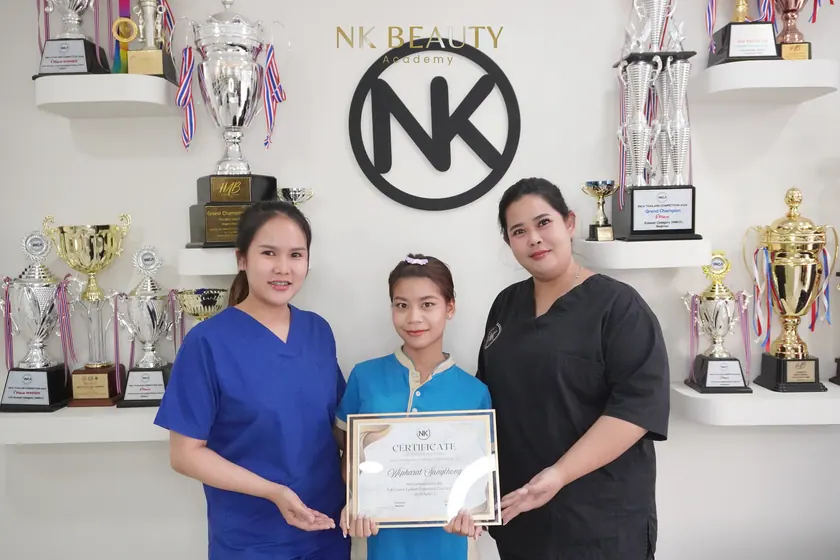 Graduates with their NK Beauty Academy certificates in front of the trophy shelves