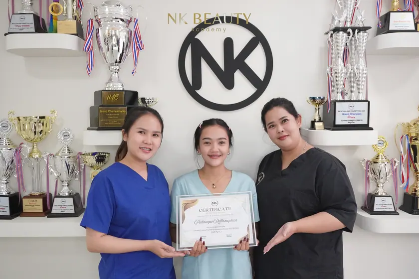 Graduates with their NK Beauty Academy certificates in front of the trophy shelves