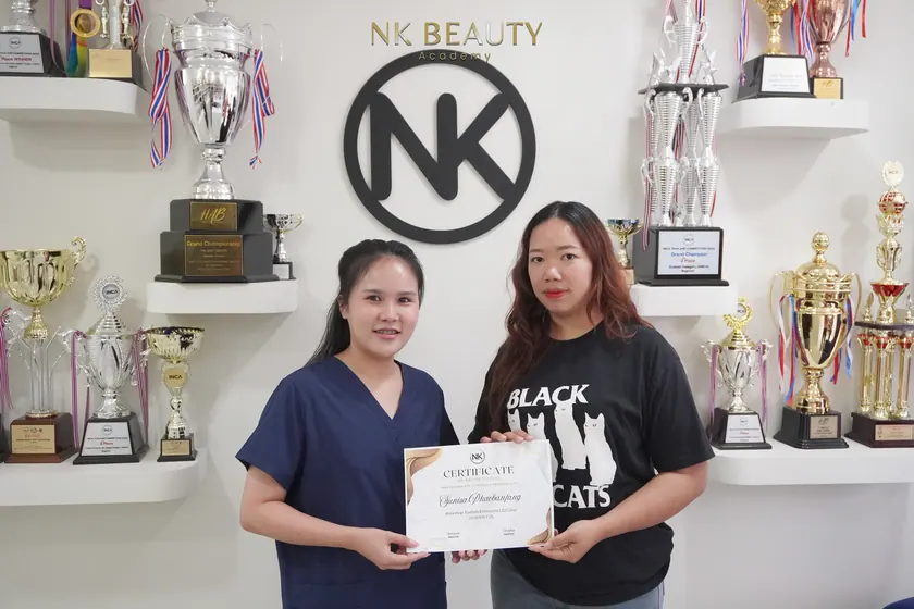 Graduates with their NK Beauty Academy certificates in front of the trophy shelves