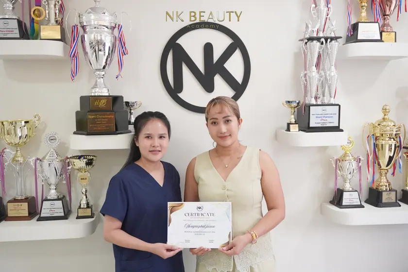 Graduates with their NK Beauty Academy certificates in front of the trophy shelves