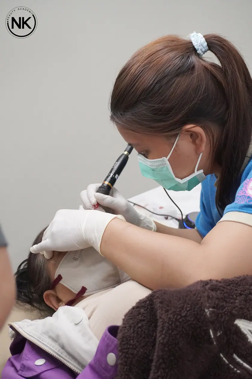 A student working with a permanent makeup machine on a live model