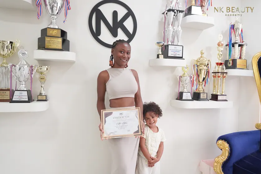 Graduates with their NK Beauty Academy certificates in front of the trophy shelves
