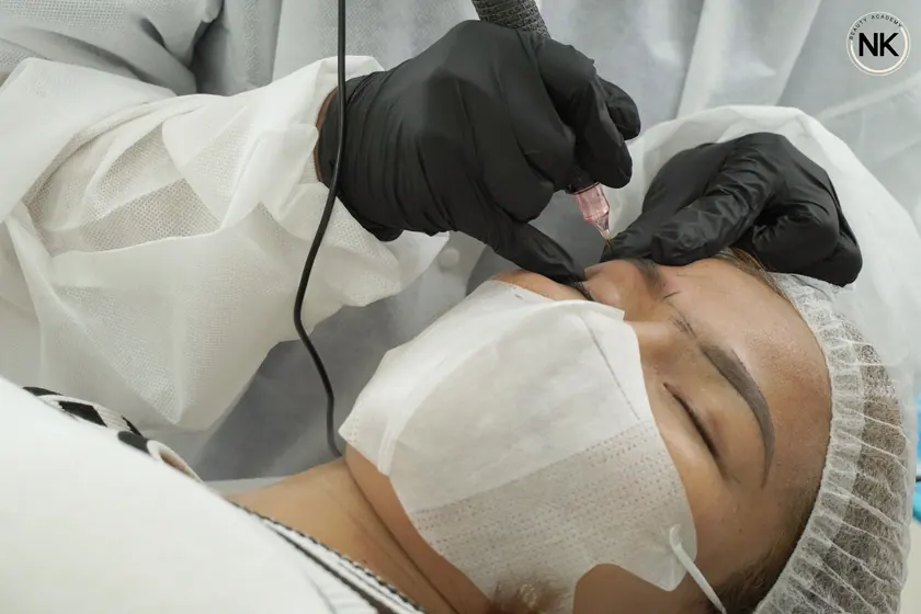A student working with a permanent makeup machine on a live model