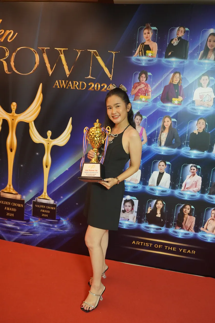 An NK Beauty artist holding a trophy in front of the Golden Crown Award backdrop