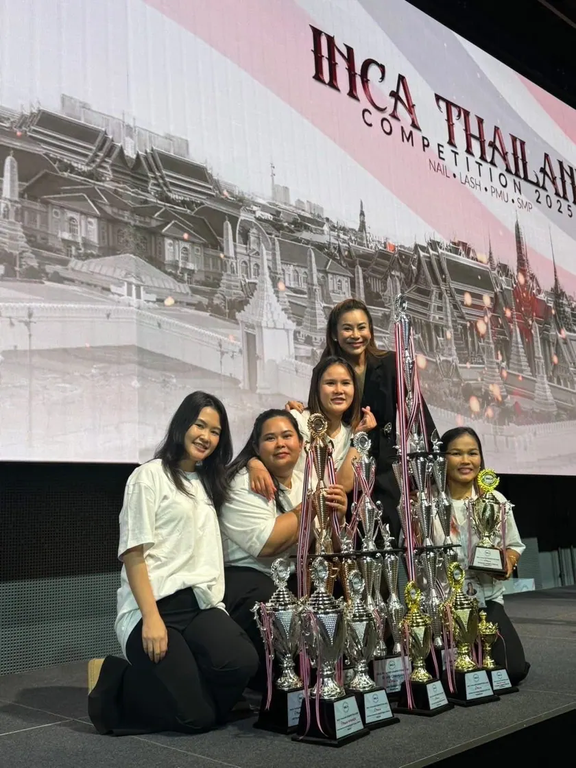 Two artists beside a stacked display of competition trophies at the INCA Thailand event